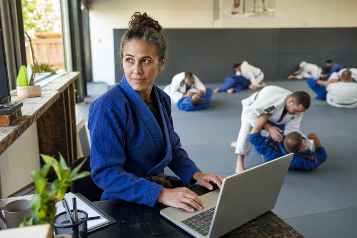 A Brazilian Jiu-Jitsu owner managing communications beside an active class